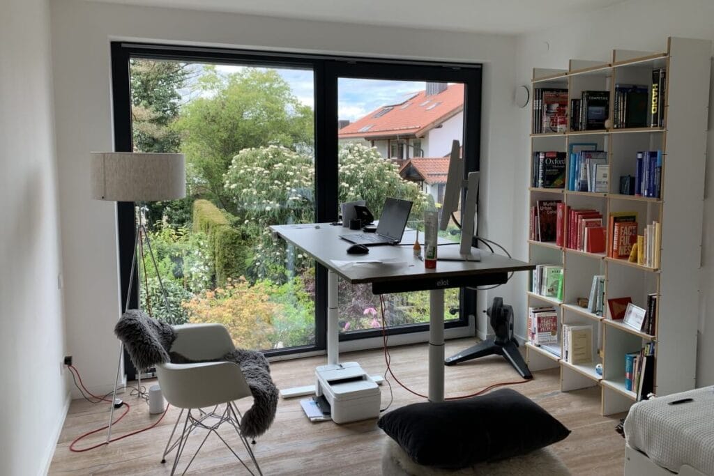 Homeoffice-Arbeitsplatz mit höhenverstellbarem Schreibtisch, Monitor, Laptop und Ausblick in den Garten – ergonomisch und modern eingerichtet